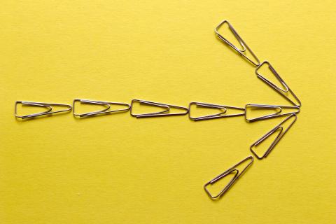 Arrow pointing to the right against a yellow background. The arrow is made of paper clips.