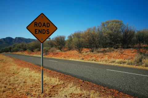 Road passing through arid land and blue sky. Sign saying 'Road Ends' alongside tarmac.