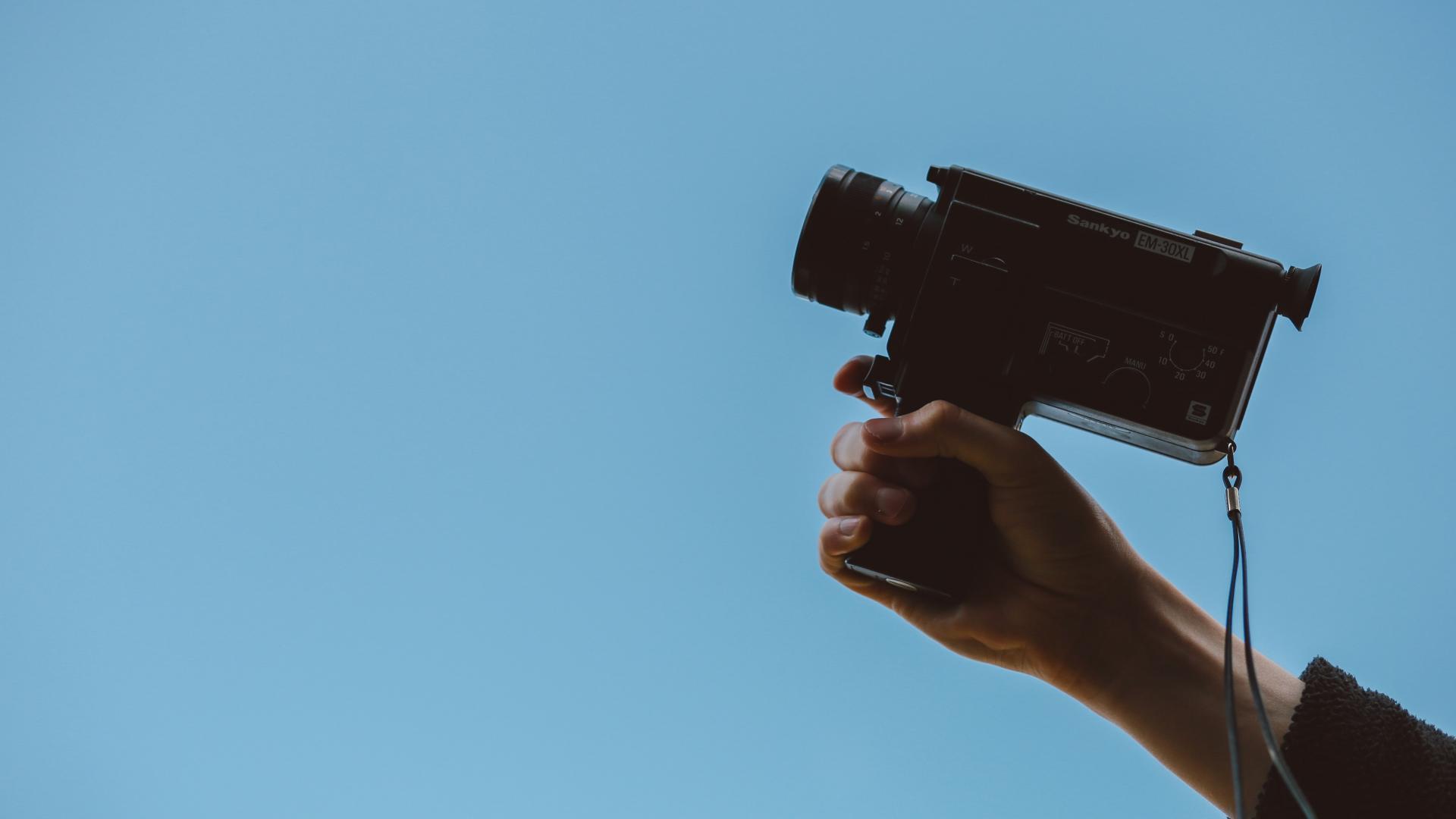 Hand holding a video camera aloft against a blue background