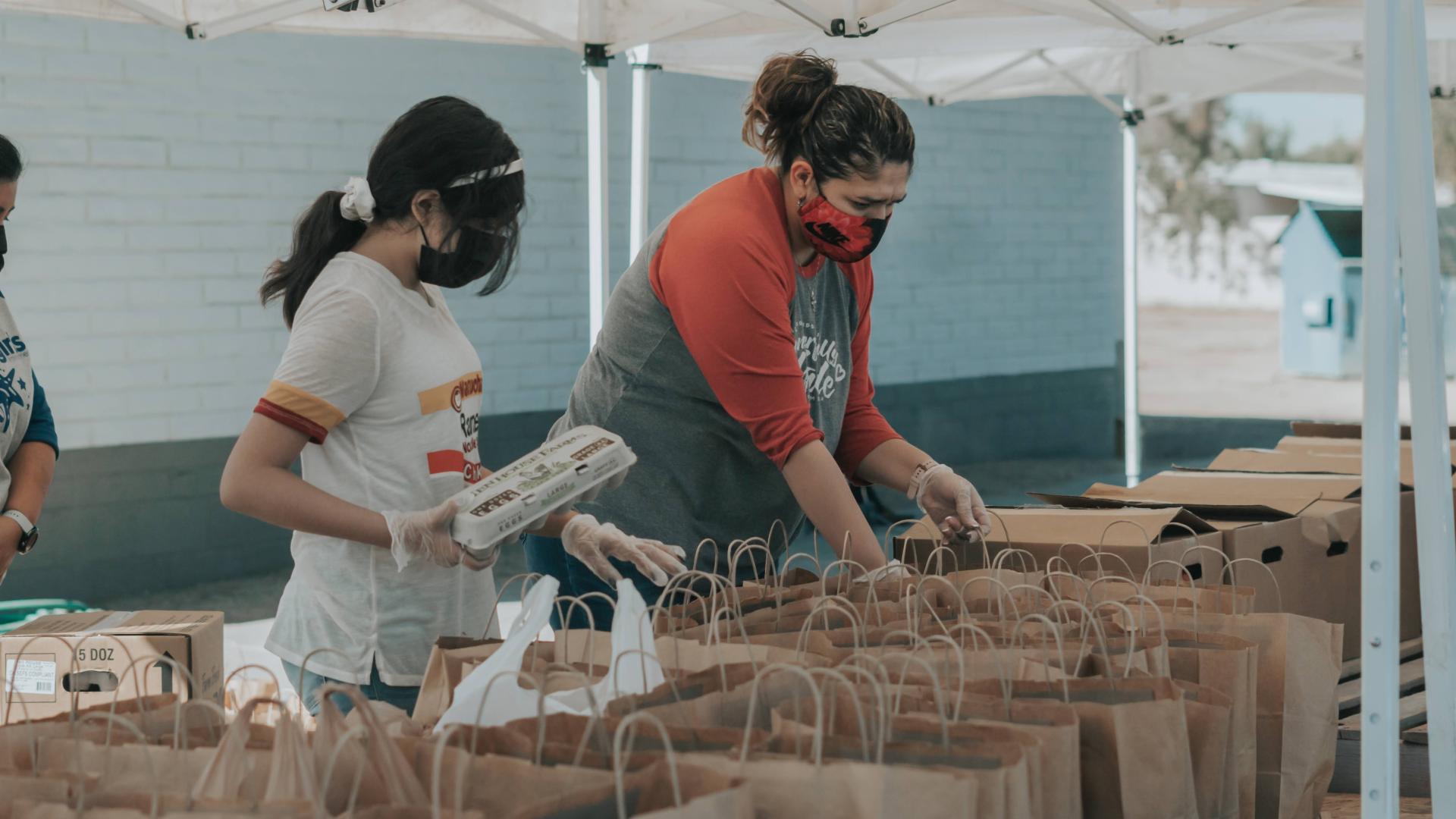 Two volunteers help sort food into paper bags